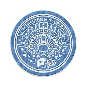 May include: A round, blue patch with white embroidered details. The text "THE PHANTOM OF THE OPERA" encircles a central design featuring a chandelier, mask, and rose. The patch has a textured appearance.