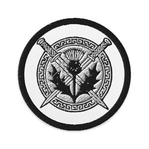 Puede incluir: Parche bordado circular con centro blanco, borde negro y costuras detalladas. El diseño presenta un cardo, espadas cruzadas y hojas de arce dentro de un borde decorativo.
