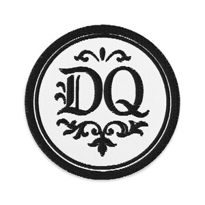May include: Embroidered patch featuring the letters "DQ" in a decorative font, surrounded by ornate floral designs. The patch has a white background with a black border and black lettering, creating a classic, elegant look.