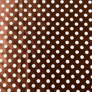 May include: Brown fabric with a pattern of evenly spaced white polka dots. The fabric has a slight sheen, and the polka dots are uniform in size and shape. The overall effect is a classic and versatile design.