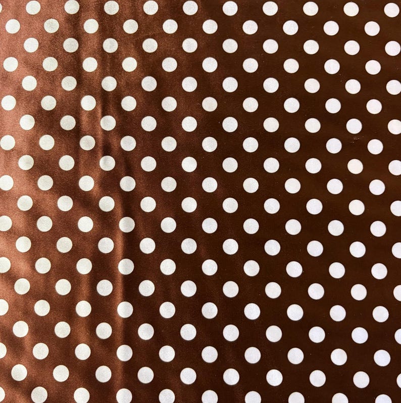 May include: Brown fabric with a pattern of evenly spaced white polka dots. The fabric has a slight sheen, and the polka dots are uniform in size and shape. The overall effect is a classic and versatile design.
