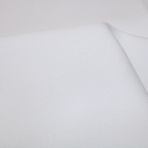 May include: White fabric with a smooth, even texture. The fabric is folded in half, creating a crease down the center.