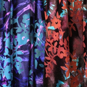 May include: Close-up of three fabric swatches with floral patterns. The fabric is a dark blue velvet with a teal and purple floral design, a dark purple velvet with a teal and purple floral design, and a dark red velvet with a teal and red floral design.