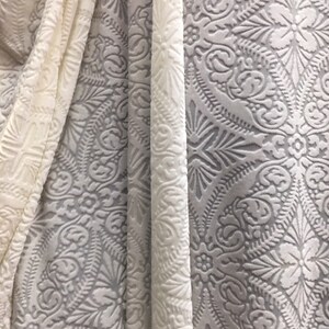 May include: Two pieces of white fabric with an embossed pattern. The fabric has a raised, textured design with a floral motif.