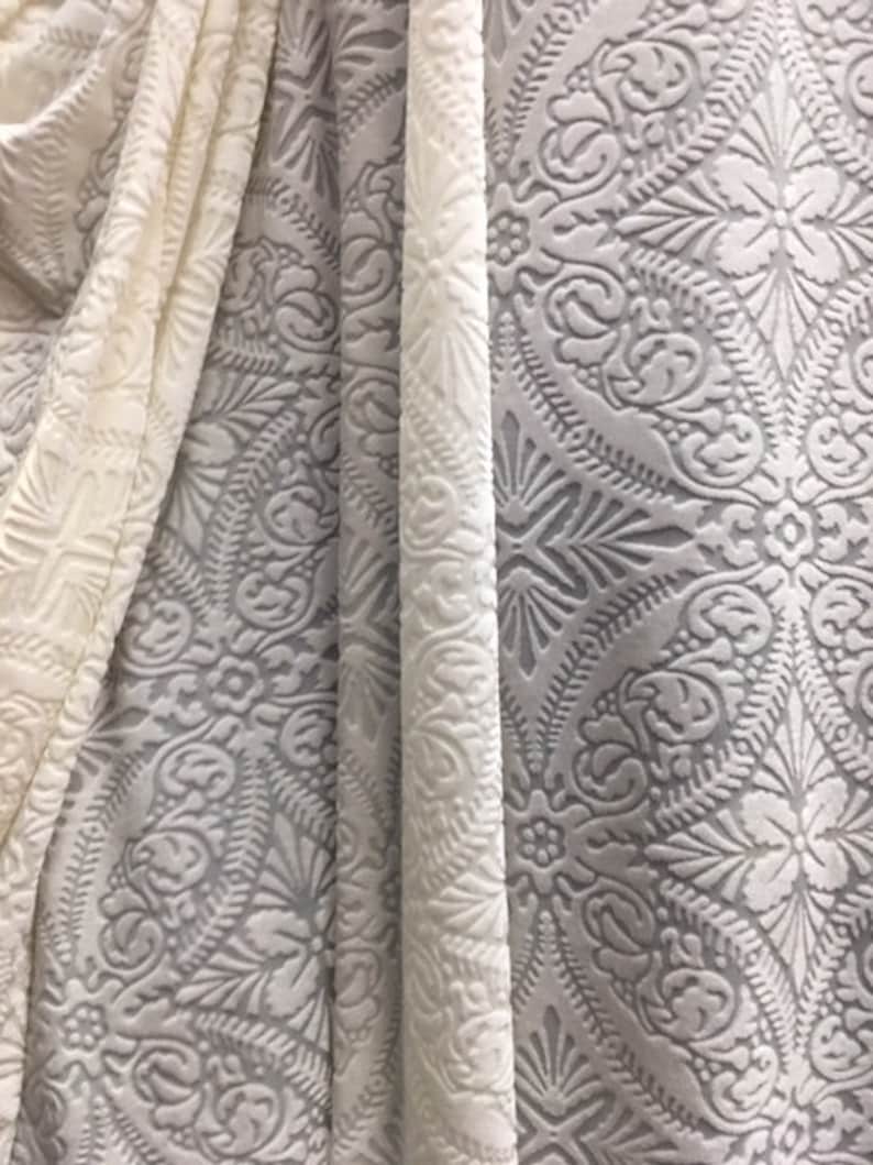 May include: Two pieces of white fabric with an embossed pattern. The fabric has a raised, textured design with a floral motif.