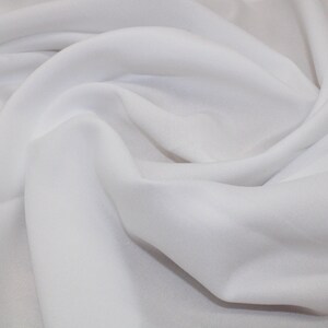 May include: White fabric with a smooth texture, folded and draped to show its soft, flowing quality.