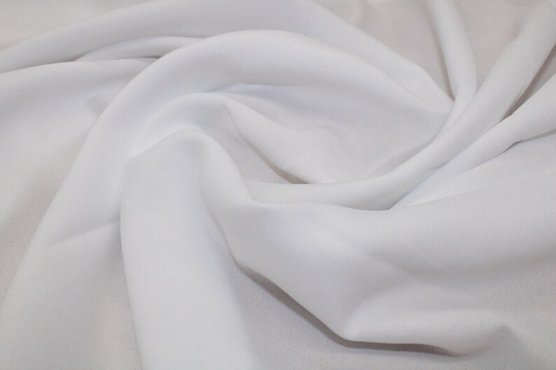 May include: White fabric with a smooth texture, folded and draped to show its soft, flowing quality.