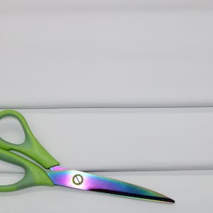 Op de afbeelding: Een schaar met groene handvatten en regenboogkleurige, iriserende bladen tegen een witte achtergrond.