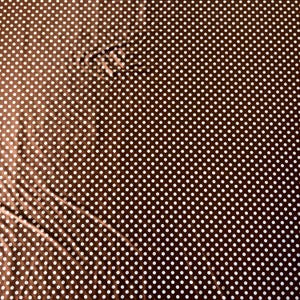 May include: Brown fabric with a white polka dot pattern. The fabric has a slight sheen and is folded in places, creating shadows and variations in the color. The polka dots are evenly spaced.