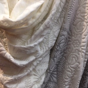 May include: Two white fabric swatches with different textures. One swatch has a smooth, plain surface, while the other has a raised, embossed pattern.