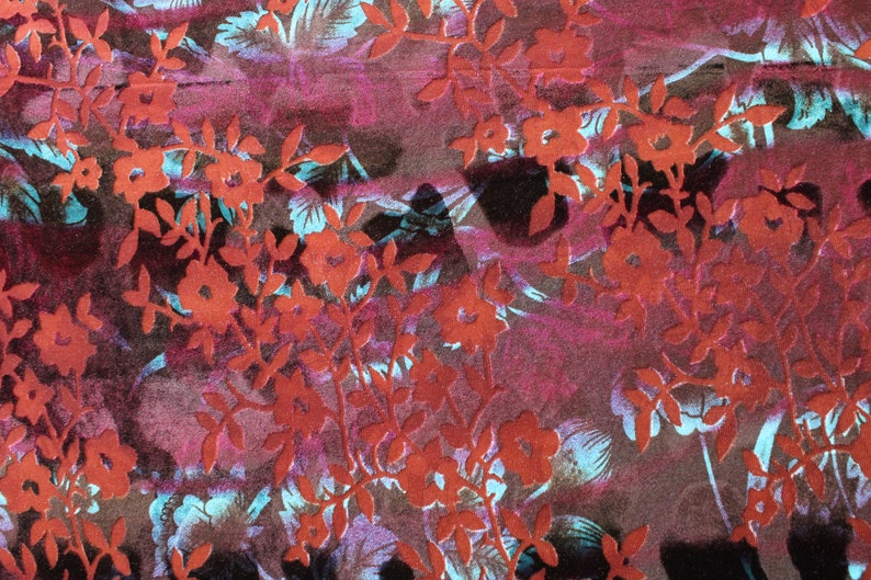 May include: A close-up of a fabric with a red floral pattern on a dark purple background. The flowers are embossed and have a 3D effect.