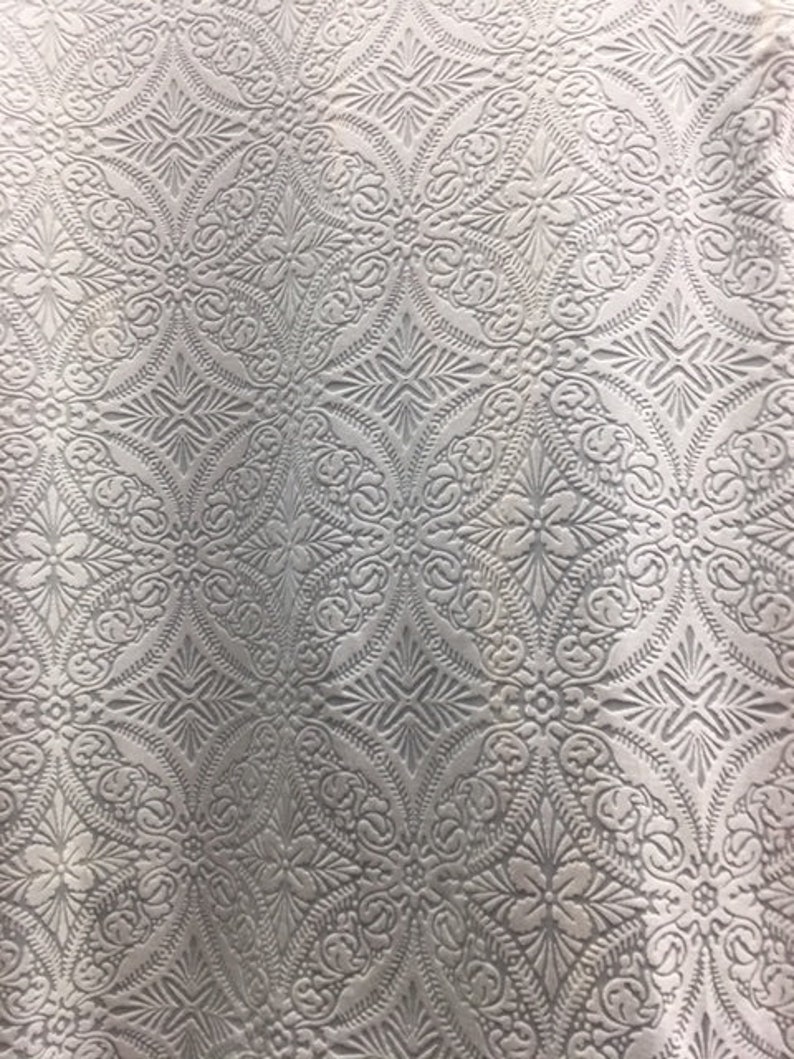 May include: White fabric with an embossed pattern of repeating geometric shapes and floral designs.