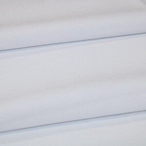 May include: White fabric folded in thirds, showing the smooth texture and subtle sheen of the material.