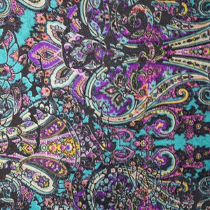 Op de afbeelding: Een kleurrijke paisley stof met een turquoise achtergrond en zwarte, paarse, roze en gele accenten.