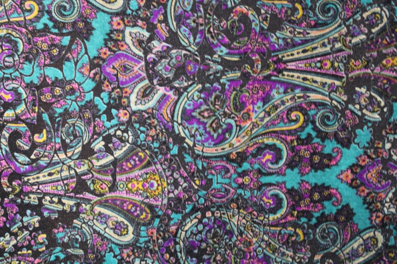 Op de afbeelding: Een kleurrijke paisley stof met een turquoise achtergrond en zwarte, paarse, roze en gele accenten.