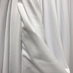 May include: White fabric with a smooth texture and a soft drape. The fabric is folded and creased, showing the natural flow of the material.