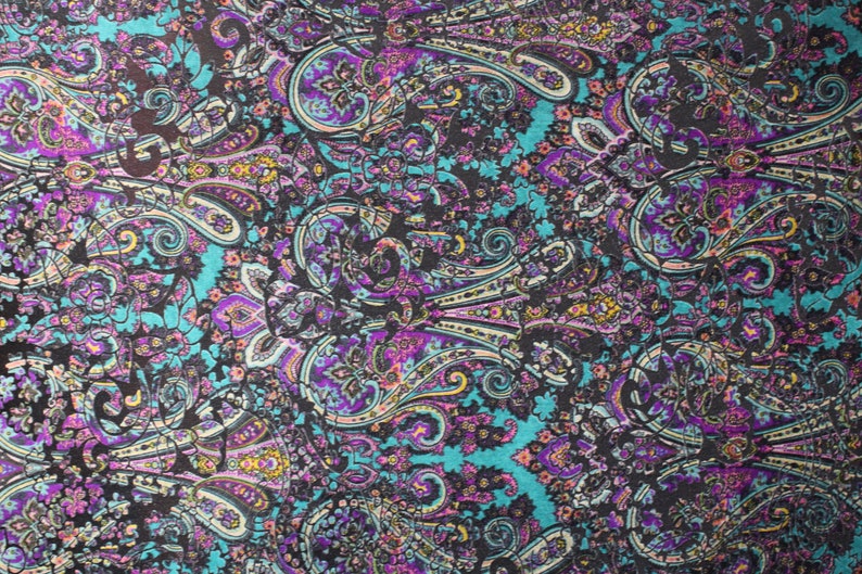 Op de afbeelding: Een tealblauwe stof met een paisley-patroon in tinten paars, roze, geel en wit.