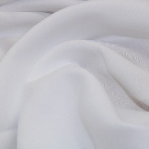 May include: White fabric with a smooth texture and a soft drape. The fabric is folded and wrinkled, creating a natural, organic look.
