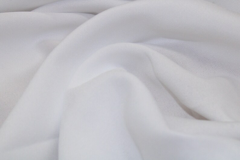 May include: White fabric with a smooth texture and a soft drape. The fabric is folded and wrinkled, creating a natural, organic look.