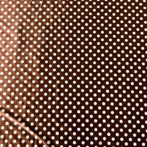 May include: Brown fabric with a repeating pattern of white polka dots. The fabric has a slight sheen, and the dots are evenly spaced across the surface. The overall effect is a classic and versatile design.