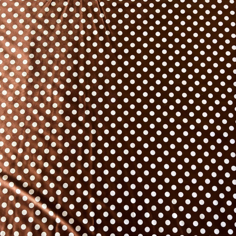 May include: Brown fabric with a repeating pattern of white polka dots. The fabric has a slight sheen, and the dots are evenly spaced across the surface. The overall effect is a classic and versatile design.