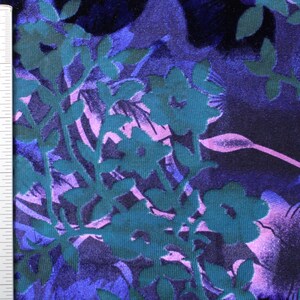 May include: A close-up of a teal, purple, and pink floral fabric with a textured, embossed design. The fabric is measured with a ruler in inches.