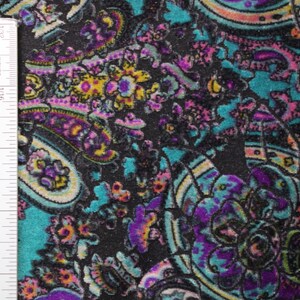 Op de afbeelding: Een close-up van een zwarte stof met een paisley-patroon in tinten roze, paars, turquoise en geel. Een liniaal is zichtbaar aan de linkerkant van de afbeelding.