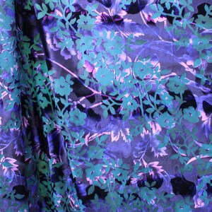 May include: A close-up of a dark blue fabric with a teal and purple floral pattern. The fabric is soft and has a subtle sheen.