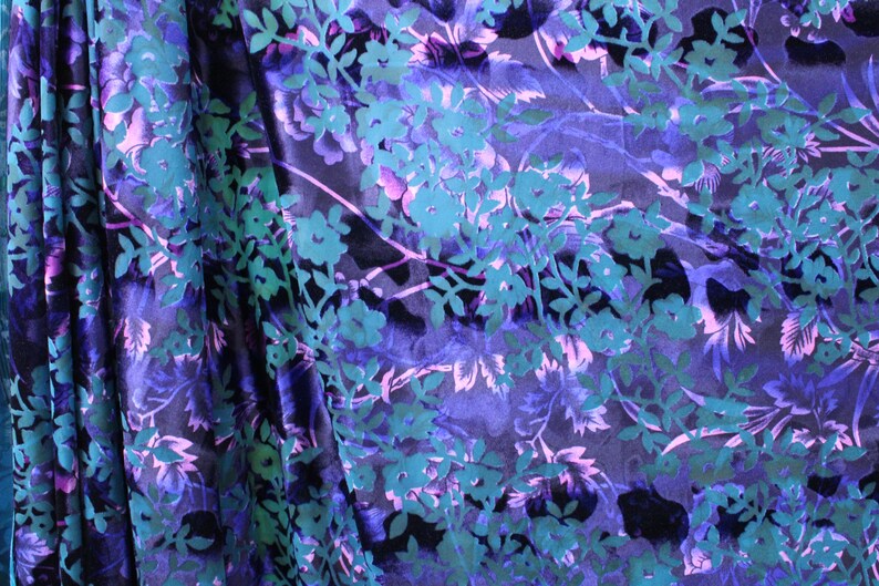 May include: A close-up of a dark blue fabric with a teal and purple floral pattern. The fabric is soft and has a subtle sheen.