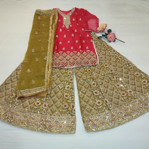 May include: A red and gold embroidered outfit, including a top, wide-leg pants, and a matching scarf. The ensemble features intricate gold detailing and embellishments. The outfit is likely for a special occasion.