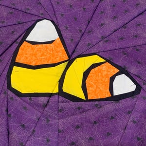 May include: Two candy corn shapes, with white, orange, and yellow segments, outlined in black, are set against a purple background with a spiderweb and spider pattern. The image is a close-up of a Halloween-themed fabric design.