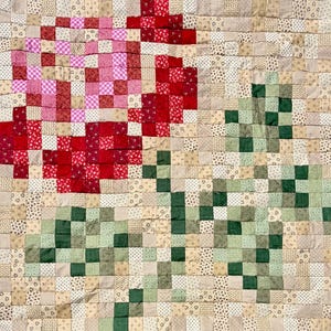 Può includere: Una trapunta patchwork con un design floreale. La trapunta presenta un motivo di quadrati rossi, rosa e verdi disposti a formare fiori e steli su uno sfondo neutro. I quadrati sono realizzati con vari tessuti fantasia.