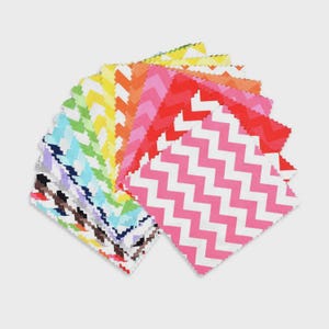 Könnte beinhalten: Eine Fächeranordnung aus bunten Papierquadraten mit verschiedenen Mustern. Die Quadrate zeigen Zickzack-Designs in Rosa, Rot, Orange, Gelb, Grün, Blau und Lila. Die Kanten der Quadrate sind mit einem dekorativen, gezackten Rand versehen.