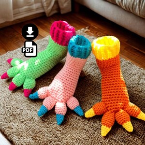 Peut inclure: Trois chaussettes en crochet en forme de pieds de monstre avec des griffes. La première est verte avec un revers et des griffes rose vif. La deuxième est rose clair avec un revers et des griffes bleus. La troisième est orange avec un revers et des griffes jaunes. Chaque chaussette possède un haut côtelé.