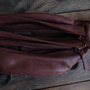 May include: A brown leather fanny pack with multiple zippered compartments. The bag is open, revealing the interior lining. The leather has a textured appearance, and the zippers are dark brown. The bag is designed to be worn around the waist.