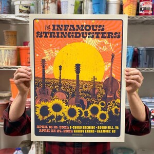 May include: Poster for The Infamous Stringdusters featuring a sunflower field with guitars, a banjo, and a double bass. The poster has a yellow and orange color scheme with the band's name at the top and concert dates and locations at the bottom.