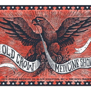 May include: A vintage-style poster with a red, white, and blue color scheme. The poster features an eagle with its wings spread wide, holding a banner that reads "Old Crow Medicine Show". The poster also includes the text "May 25, 2015 | Pisgah Brewing Co | Black Mountain, NC | w/ The Devil Makes Three".