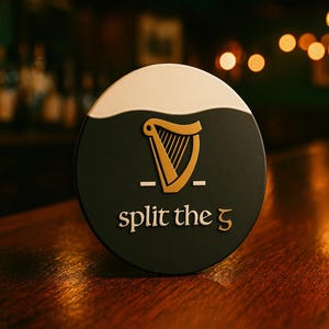 Op de afbeelding: Een ronde, donkergroene bierviltje met een witte bovenkant en een gouden harp-logo. De tekst "split the 5" is in goud. De bierviltje ligt op een houten bar.