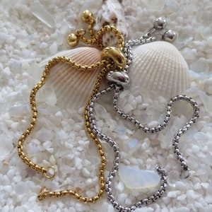 May include: Two adjustable chain bracelets, one gold and one silver, with a decorative clasp. The bracelets are displayed on a white background with seashells.