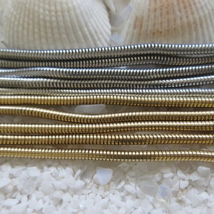 May include: Close-up of multiple silver and gold snake chains. The chains are arranged in rows, with the silver chains on top and the gold chains on the bottom.