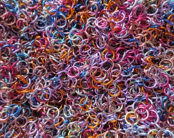 May include: A close-up of a large pile of colorful metal jump rings. The rings are in shades of purple, blue, orange, and gold.