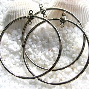 May include: Three silver metal hoops with a seashell charm on each hoop. The hoops are stacked on top of each other and are on a white background.