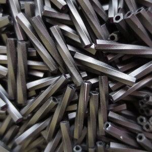 May include: A close-up image of a pile of black hexagonal beads. The beads are made of a smooth, shiny material and have a slightly iridescent finish.