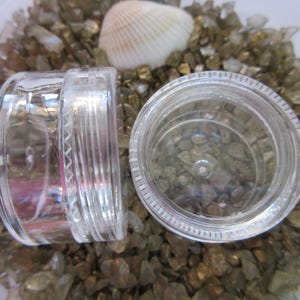 May include: Two clear plastic containers with lids, one is slightly larger than the other. The containers are sitting on a bed of small, gold-colored stones.