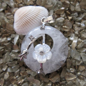 May include: A white quartz pendant with a silver flower charm and a silver branch design. The pendant is on a white background.