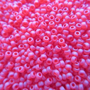May include: A close-up image of a large quantity of small, pink, round beads. The beads have a slightly iridescent finish.
