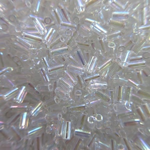 May include: A close-up image of a pile of iridescent glass beads. The beads are small and cylindrical, with a clear, translucent color. They have a subtle rainbow sheen.