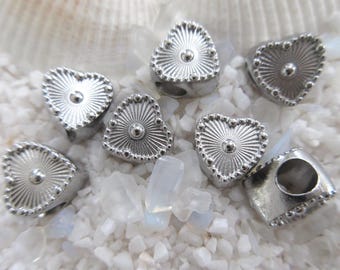 May include: Six silver heart-shaped beads with a raised, textured design. The beads have a small, round stud in the center of each heart.