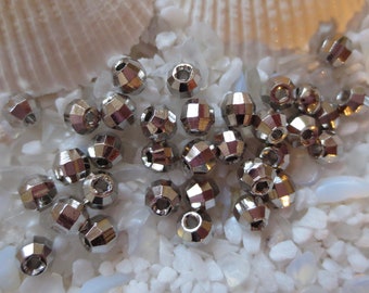 May include: A close-up of a pile of silver-toned faceted beads. The beads are round and have a hole in the center. They are scattered on a white surface.