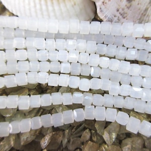 May include: A strand of white, square-shaped beads. The beads are made of a translucent material and have a slightly iridescent sheen.